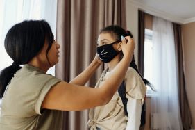 Mother helping daughter put on a face mask