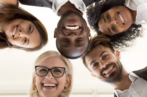 Five diverse people standing over the camer looking down and smiling