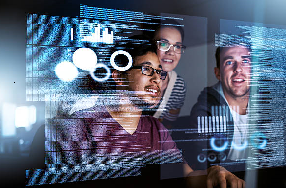 Three people looking at a screen in the dark with code displaying on the screen