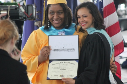 Photo of a girl in a cap and gown recieving her diploma from a woman at graduation Photo of a girl in a cap and gown recieving her diploma from a woman at graduation