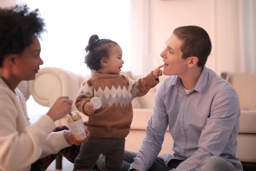 Family in living room: baby playing with father while mother feeds baby