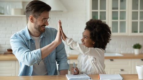 Man high-fiving girl as she does her homework