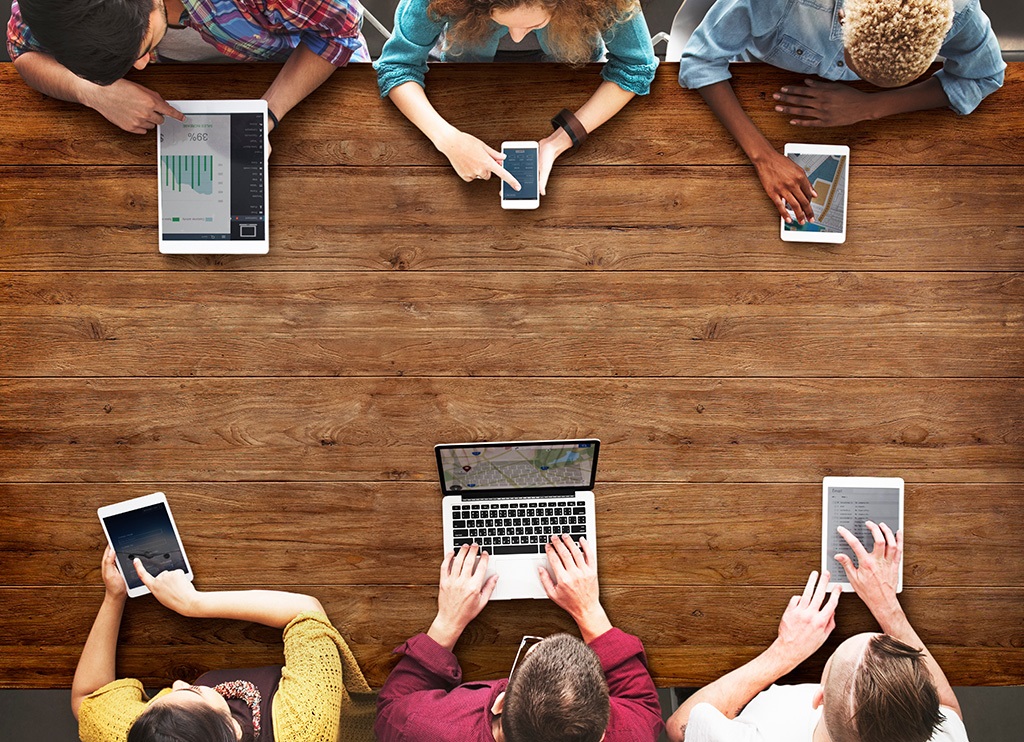 People sitting on a table and working with phones, tablets, and laptops