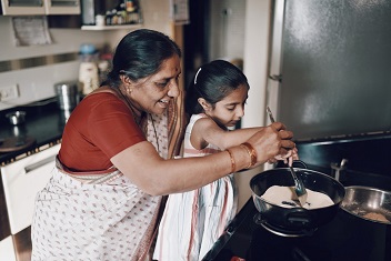 Grandmother and granddaughter stirring ingredients in a pot on the stove.